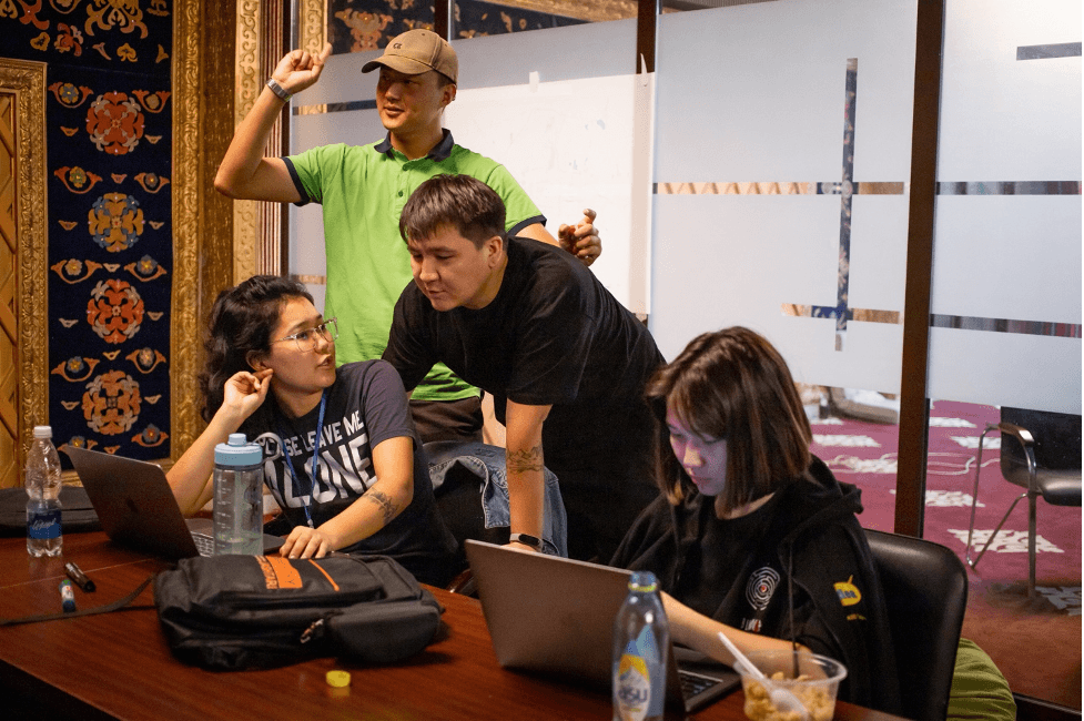 A group of people sitting around a table with laptops